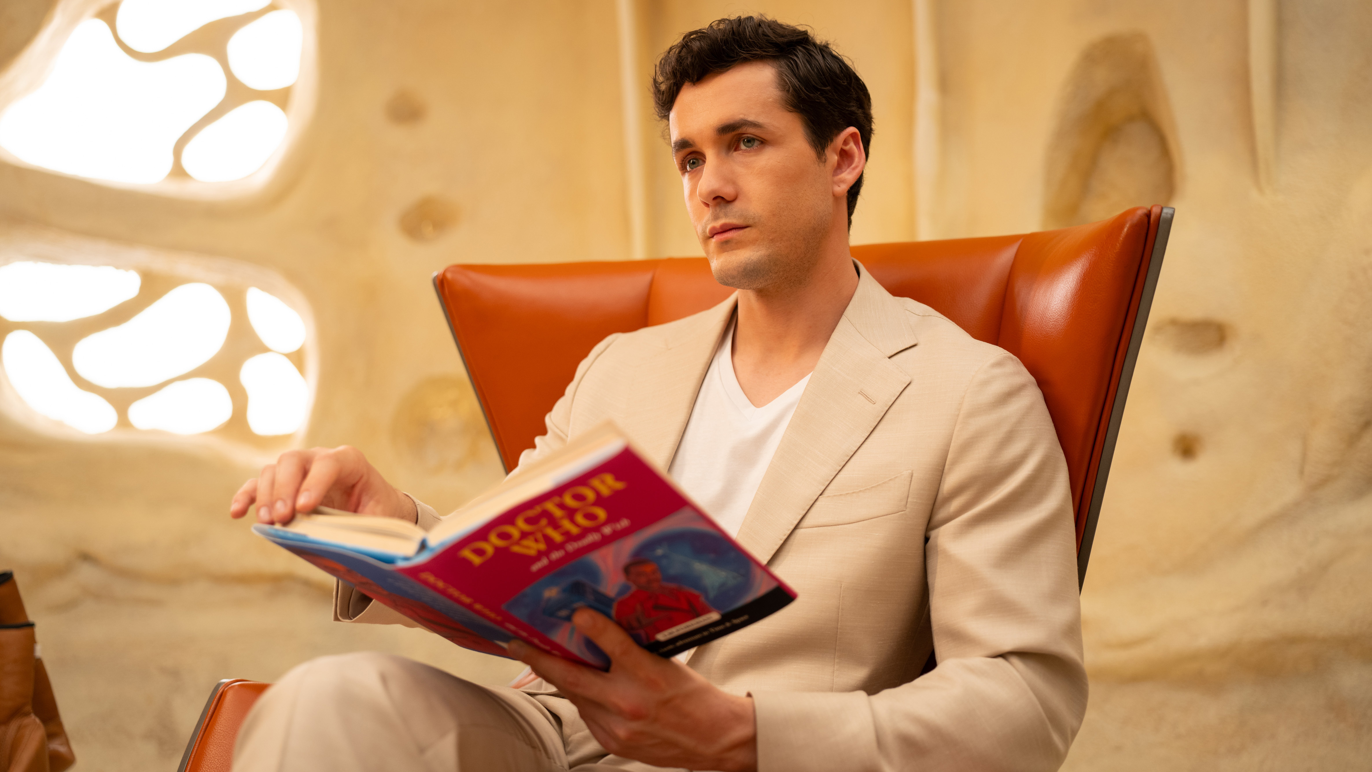 Jonah Hauer-King as Conrad, reading a book titled Doctor Who and the Deadly Wish in Doctor Who: 'Wish World.'