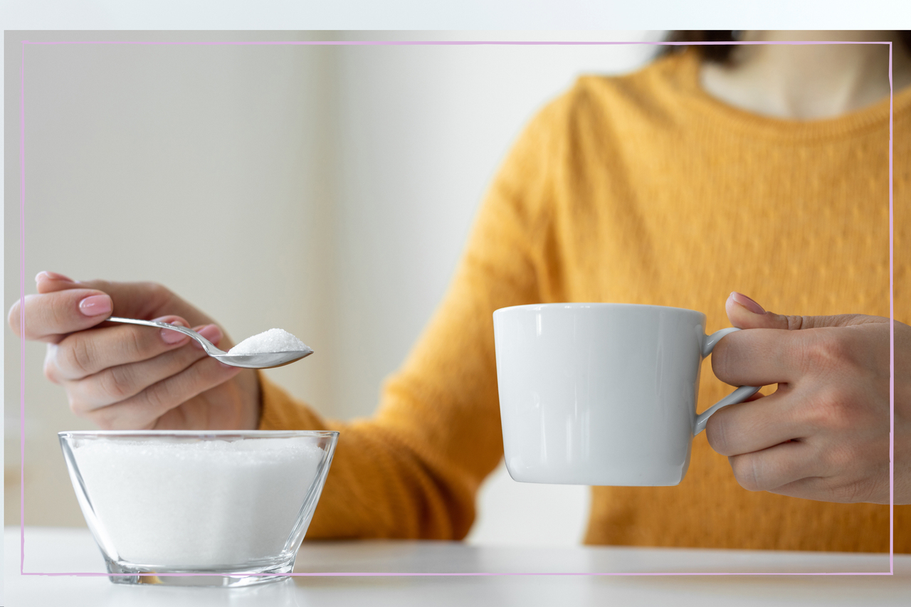 Woman in a yellow jump spooning sugar into her tea 