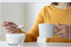 Woman in a yellow jump spooning sugar into her tea 