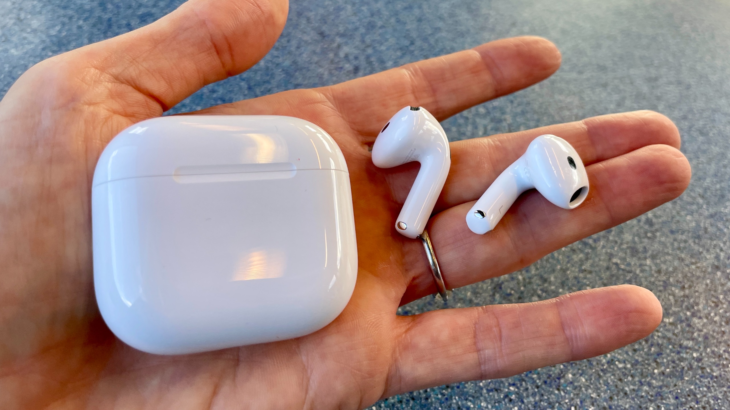 Apple AirPods 5 with Wireless Charging, on a blue table and held in a hand