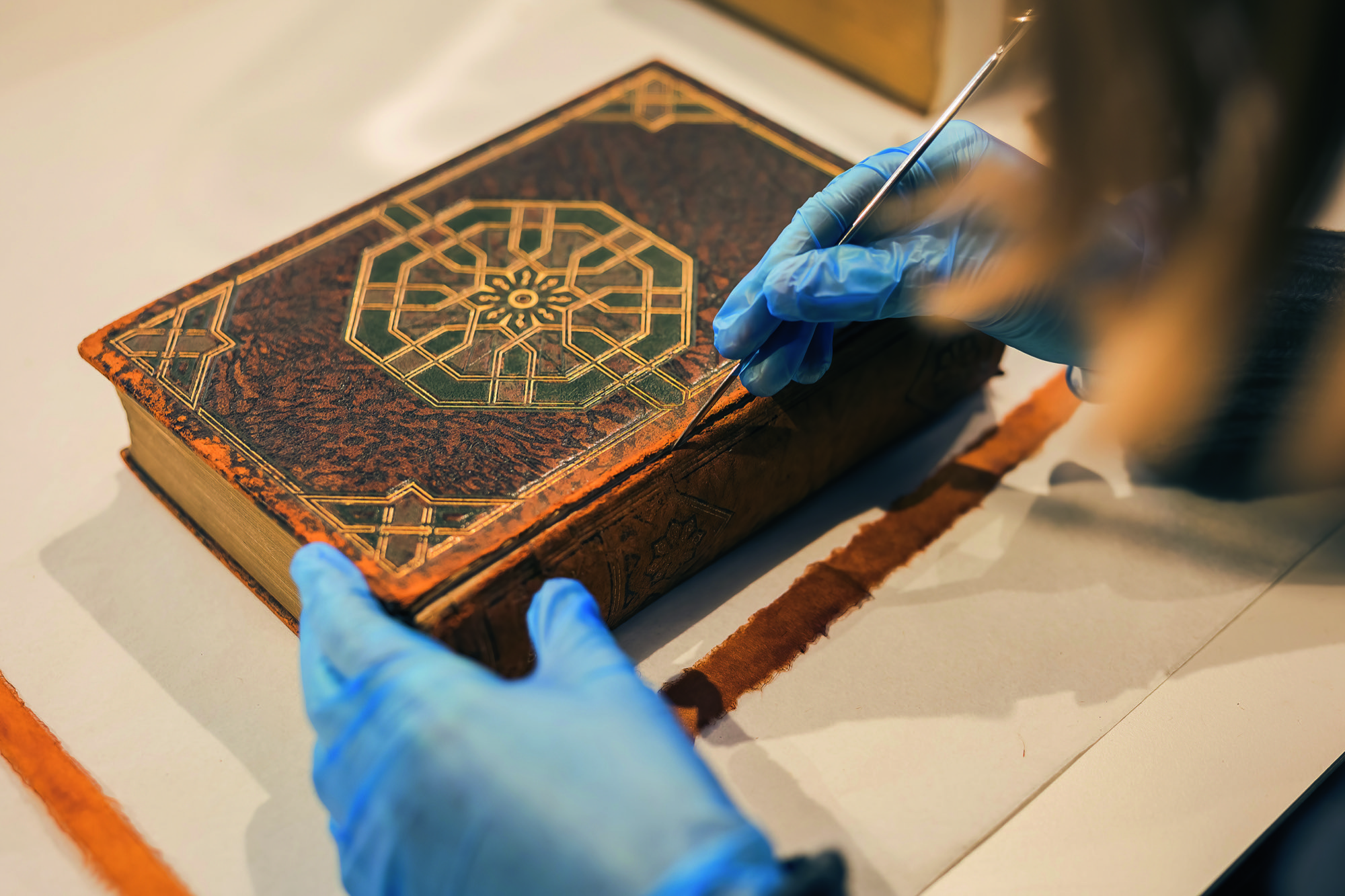 A woman in blue gloves tends to a leather book with a small scalpel