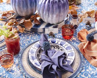 Thanksgiving centerpiece ideas with blue and white patterned tablecloth, autumn leaves and blue pumpkin decorations