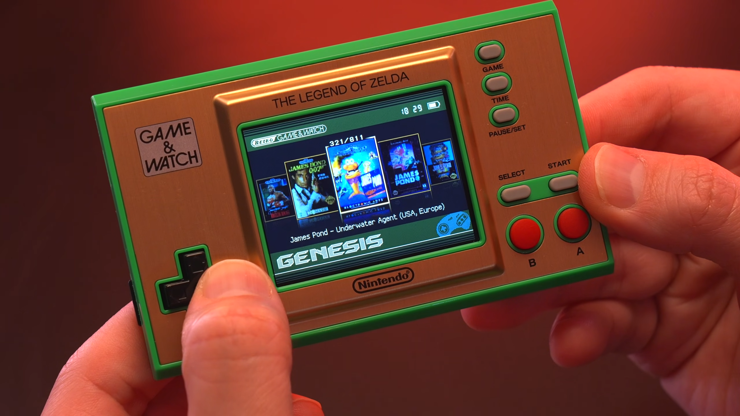 Screenshot of modded Zelda Game and Watch featured in Macho Nacho Productions with game library on screen and hands scrolling through Sega Genesis games.