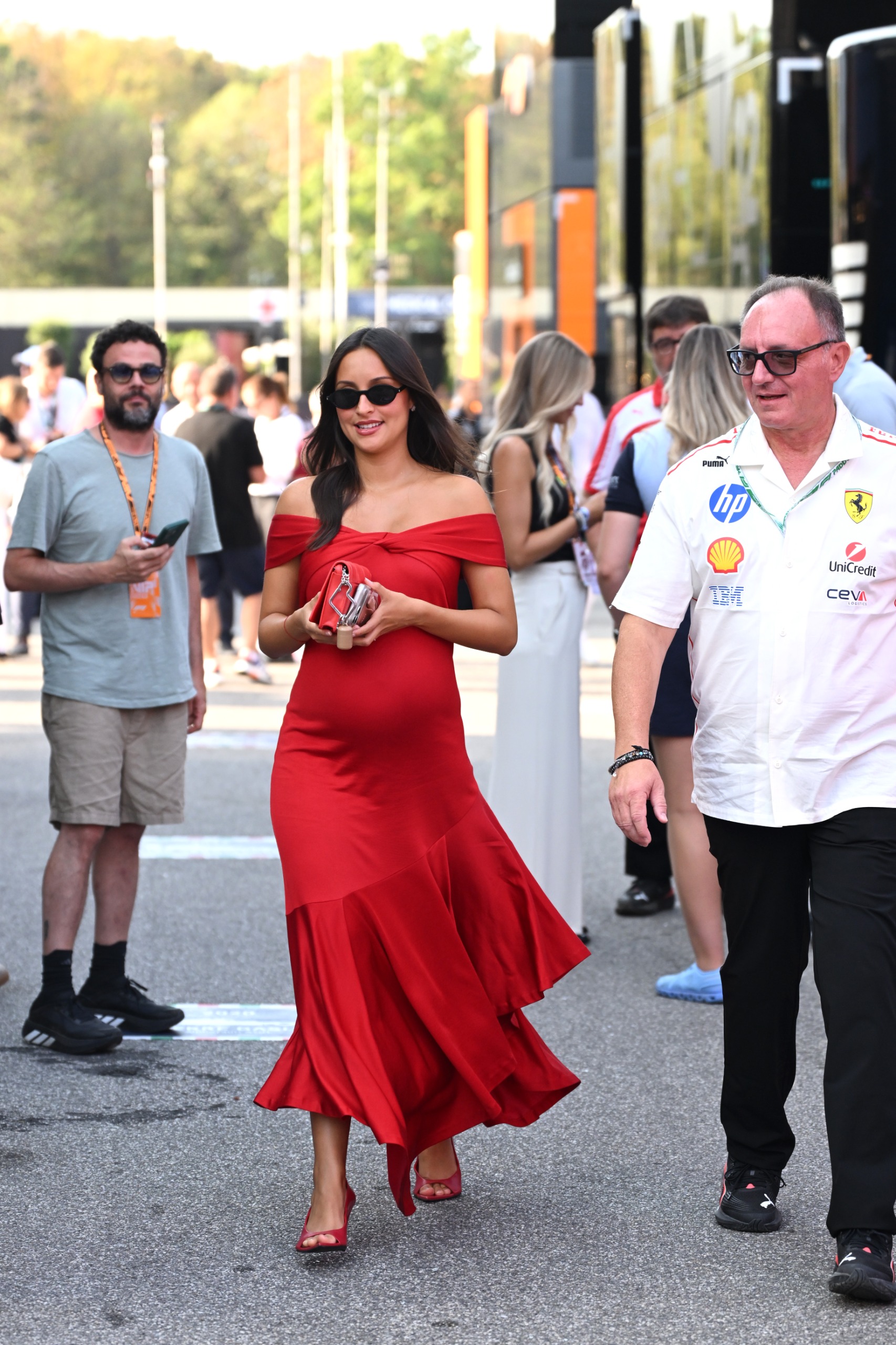 Alexandra Leclerc wearing a red Ferrari dress, she has long brown hair and is pregnant while wearing sunglasses