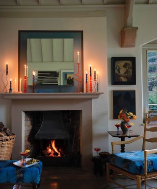 cozy living room with open fire, candles lit on mantle, log basket, armchair, mirror, artwork, Farrow & Ball