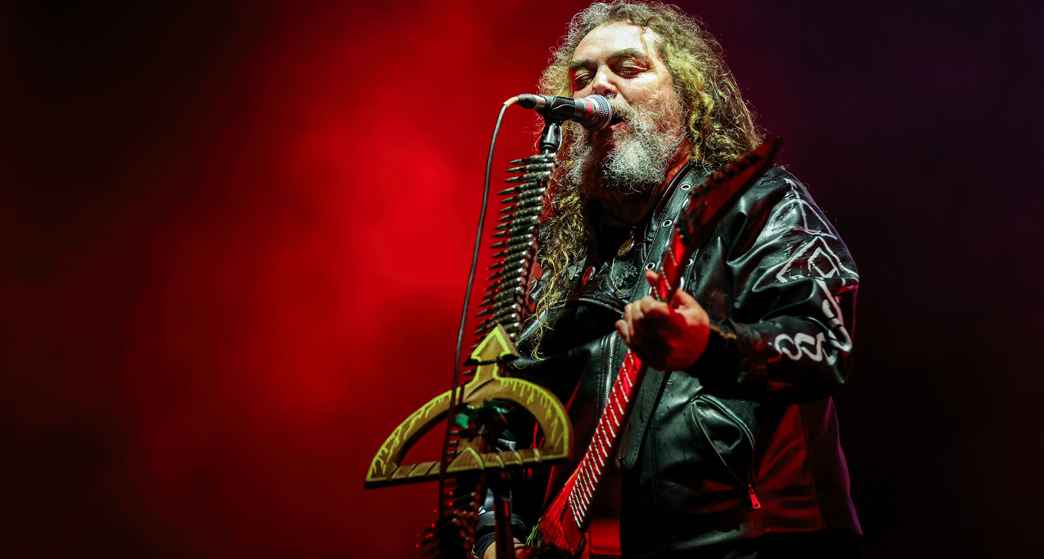 Max Cavalera performs live with a V-style electric guitar and a mic stand decorated with bullets.