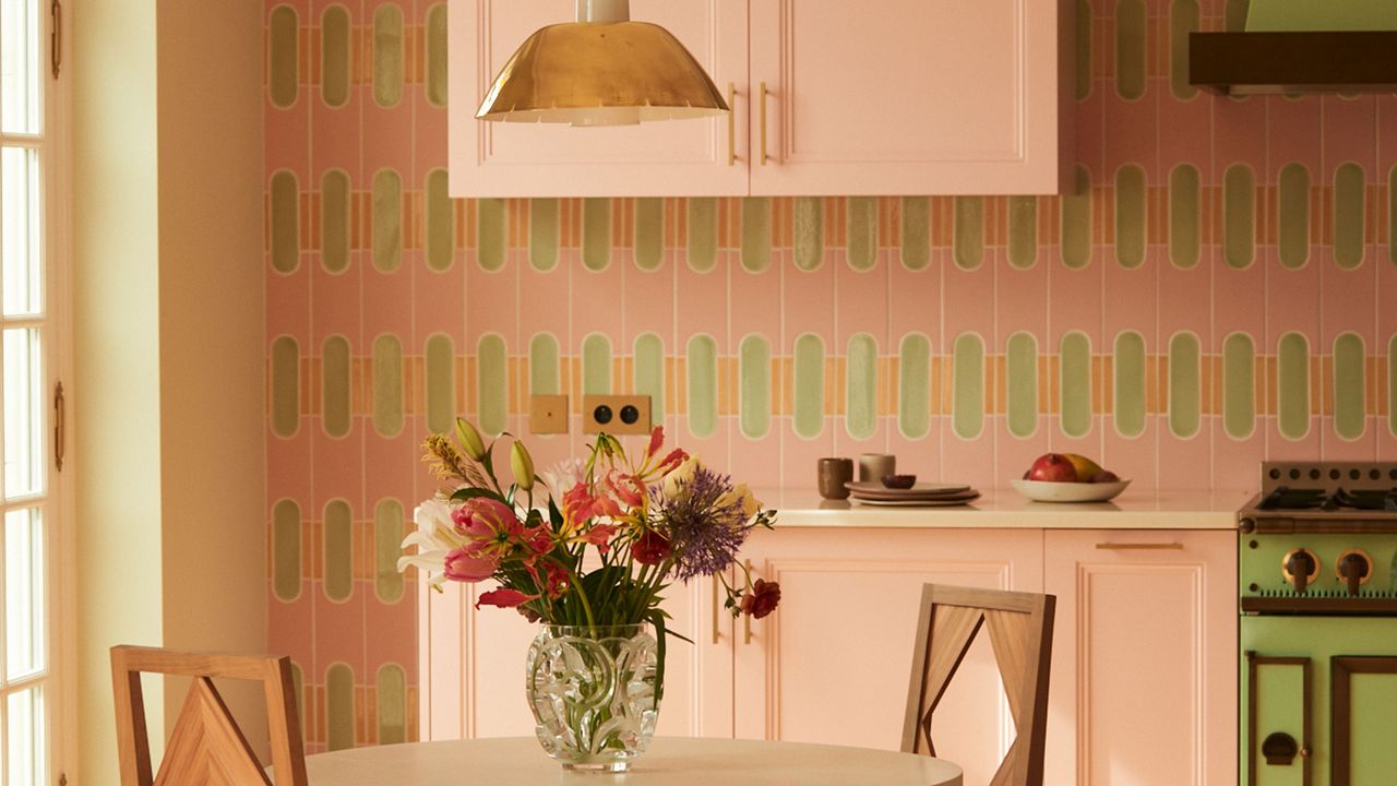 a pink and green kitchen with patterned tiles and flowers on a table