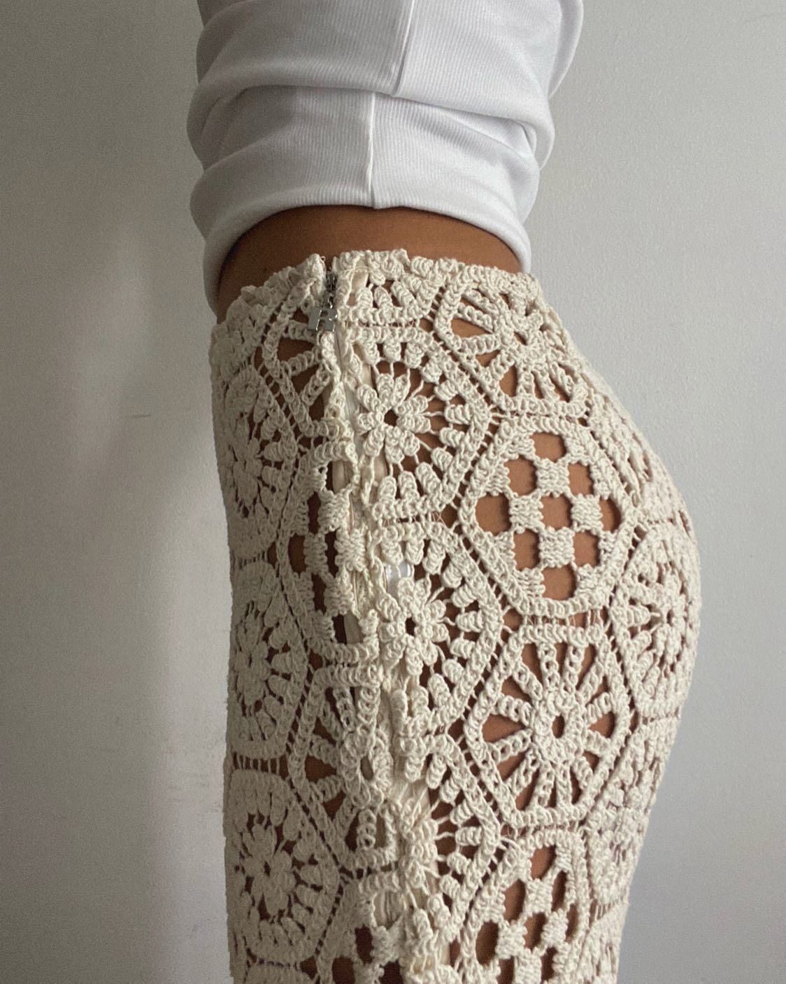 Style influencer Debora Rosa poses for a cropped outfit photo with a white top and beige crochet pants