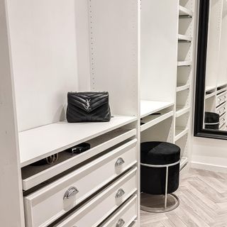 a black handbag on the shelf of a white walk in wardrobe with a black stool and wood floor