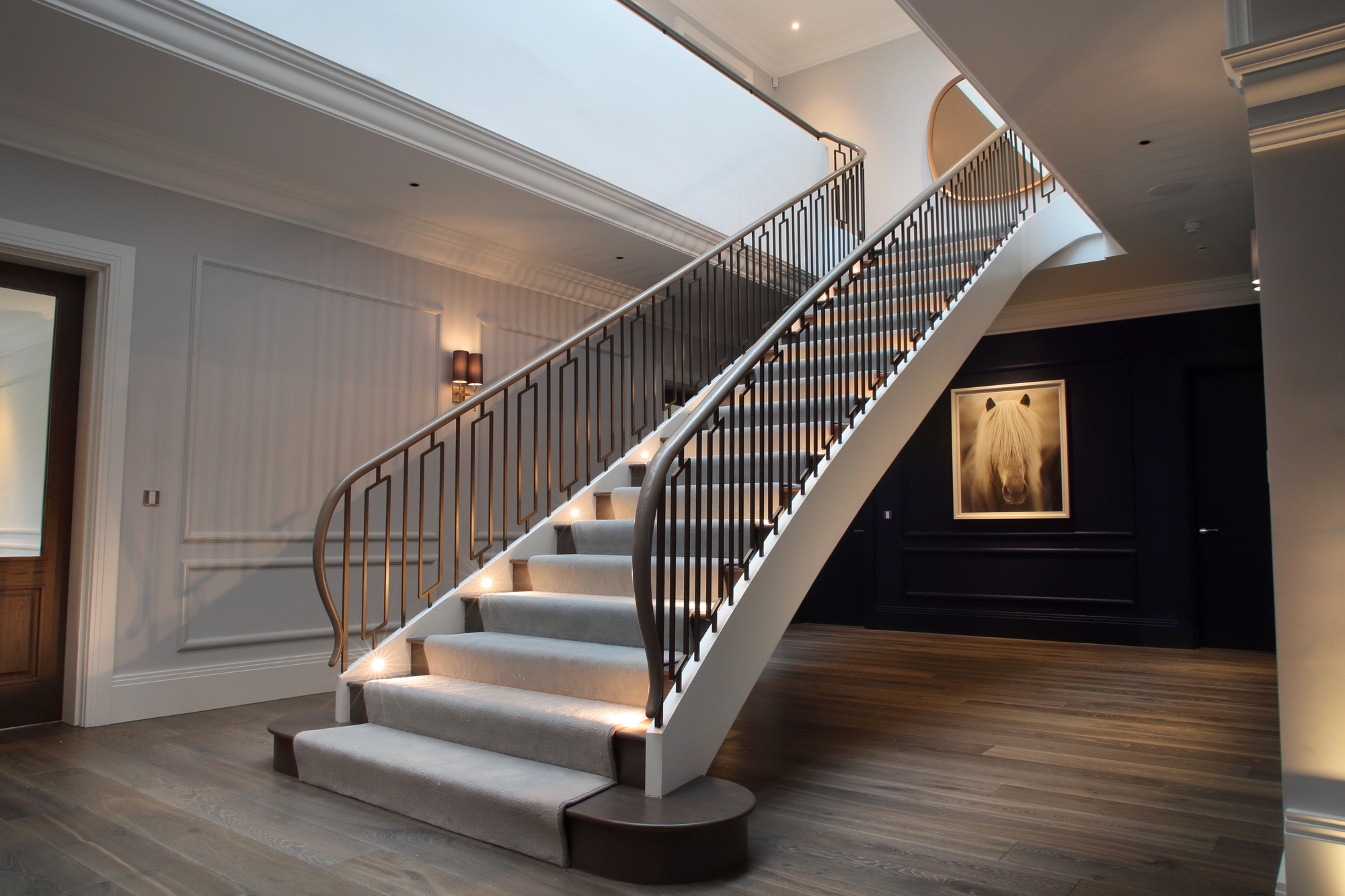 A large entryway with a grand staircase with every other riser lit by a recessed spotlight