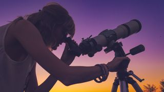 Girl looking through telescope on tripod at sunset