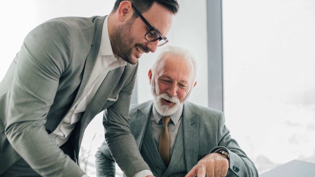 Older and younger white men in suits talking business