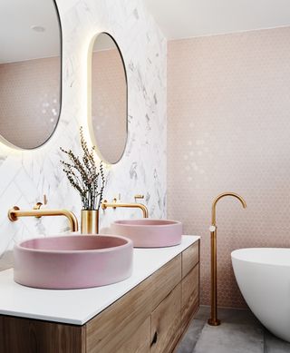 Norsu pink bathroom idea with twin round basins and brass taps with two round mirrors and freestanding white bath