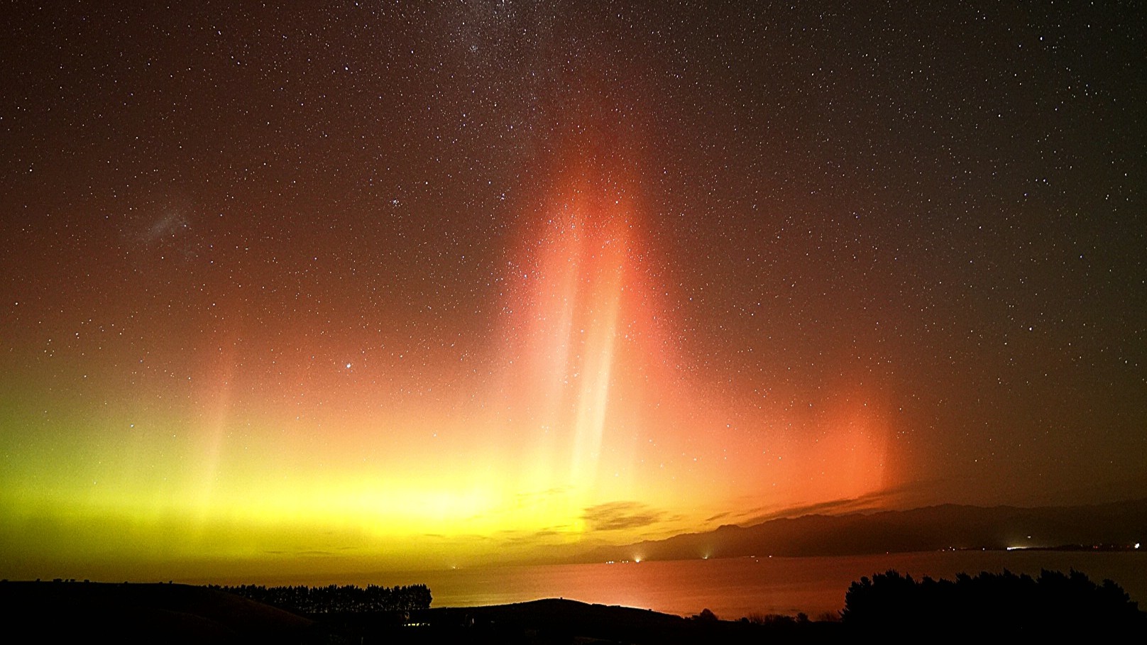 auroras reaching high into the sky colored orange and yellow. Tall pillars of light are seen across a star studded sky.