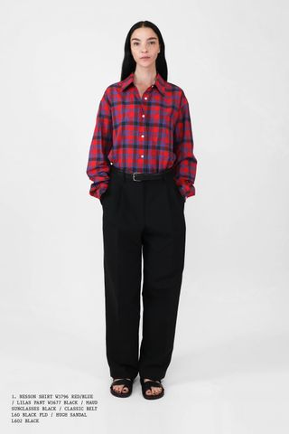 The Row Spring 2025 model in a flannels outfit of a red and blue plaid shirt, black pants, and open-toed sandals.