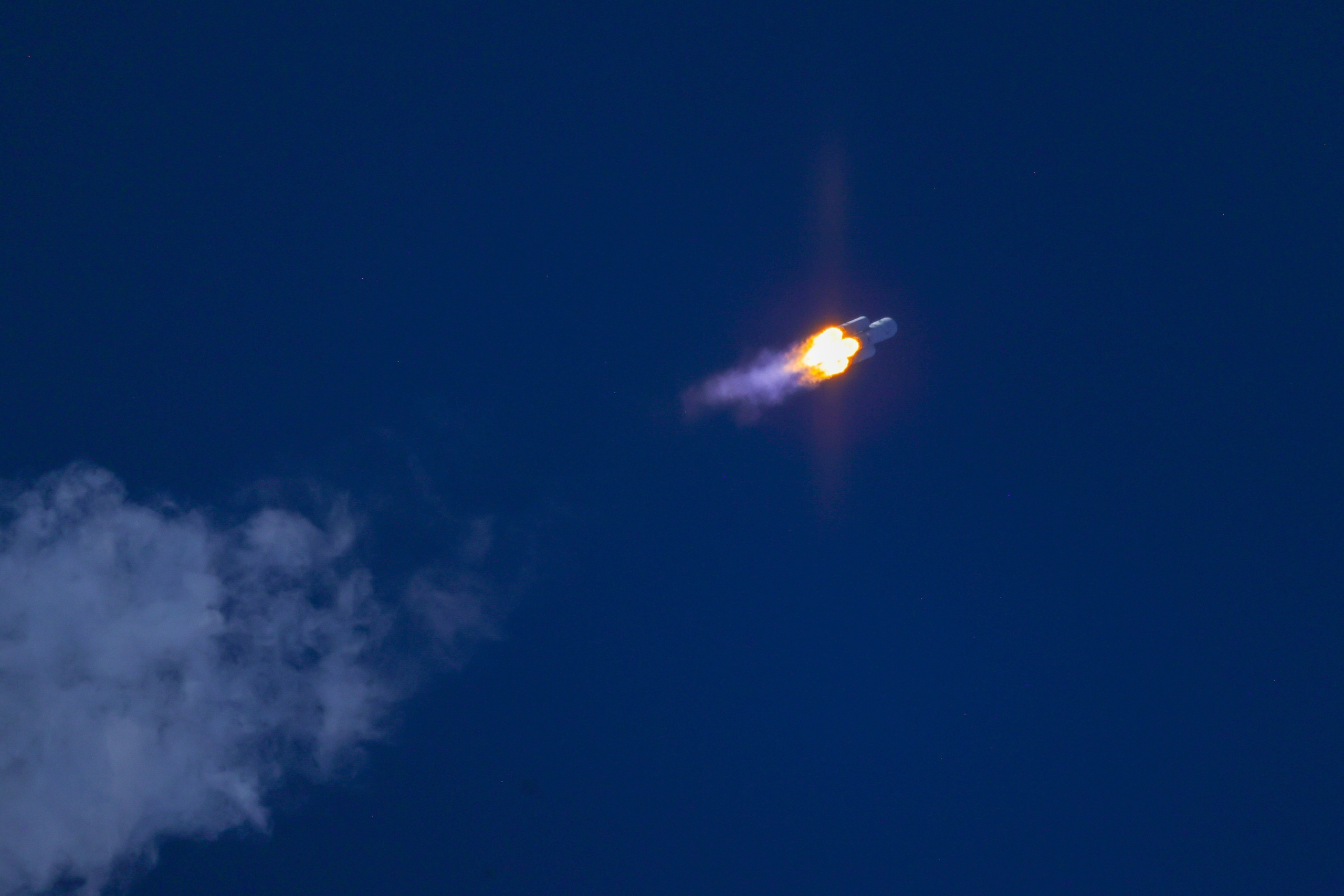 a large white rocket with four smaller boosters lifts off above a plume of fire
