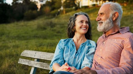 A mature, retired couple sit on a park bench.