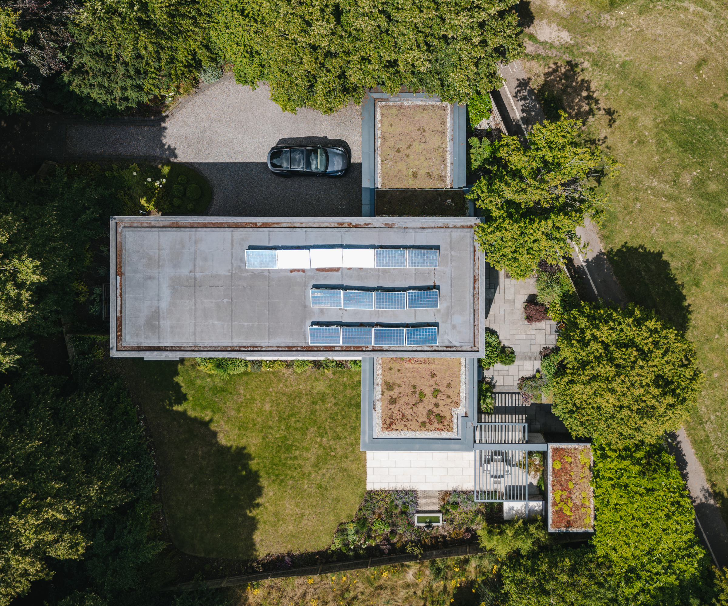 Birds eye view of the top of the house which is fitted with solar panels, and surrounded by grass and trees