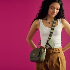 Model on hot pink background with a brown Kate Spade cross-body bag