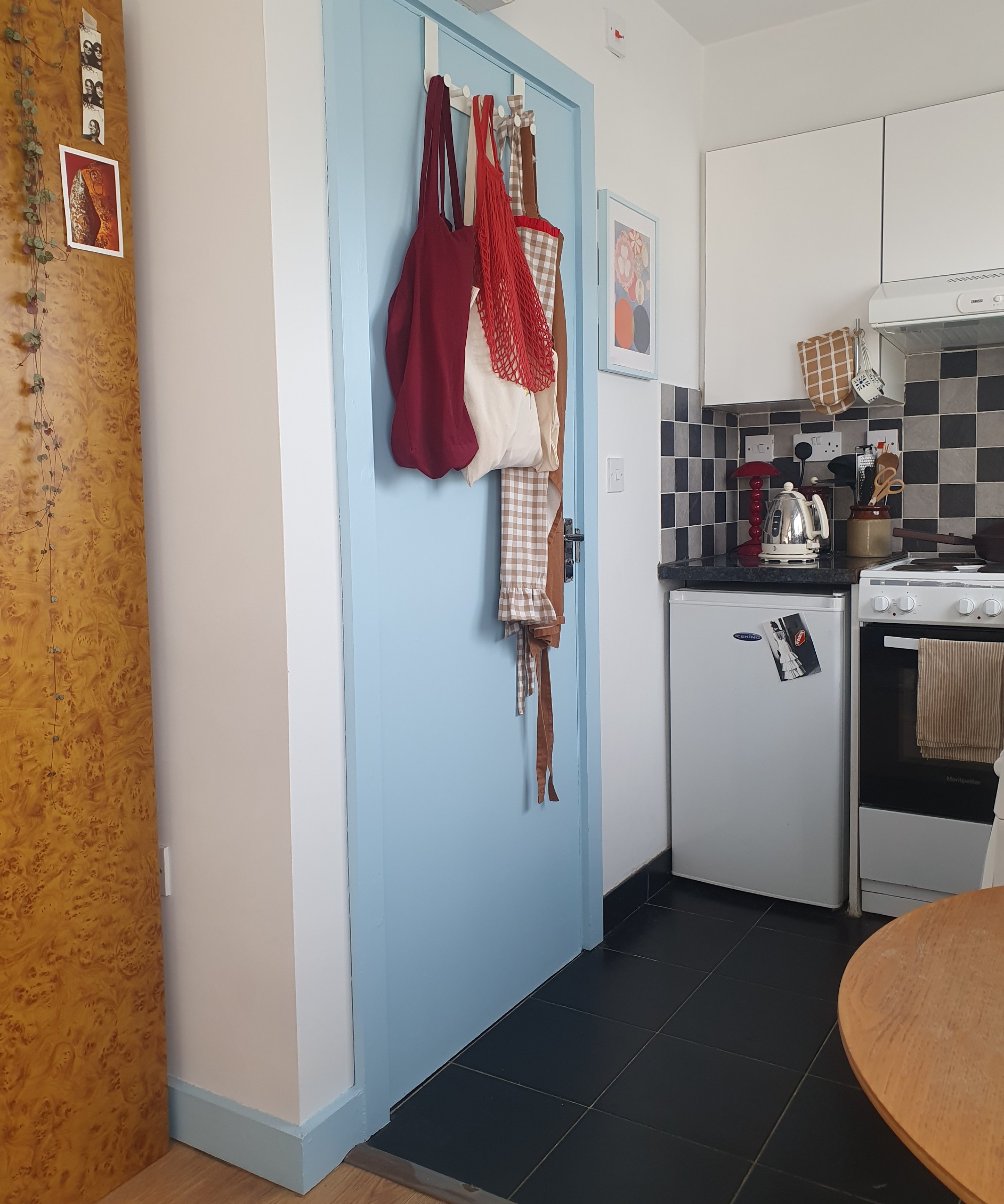 A small white kitchen with black floor tiles and a sky blue door with matching skirting boards