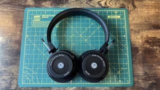Grado's GW100x headphones in a green-walled room, on a wooden desk with cutting mat.