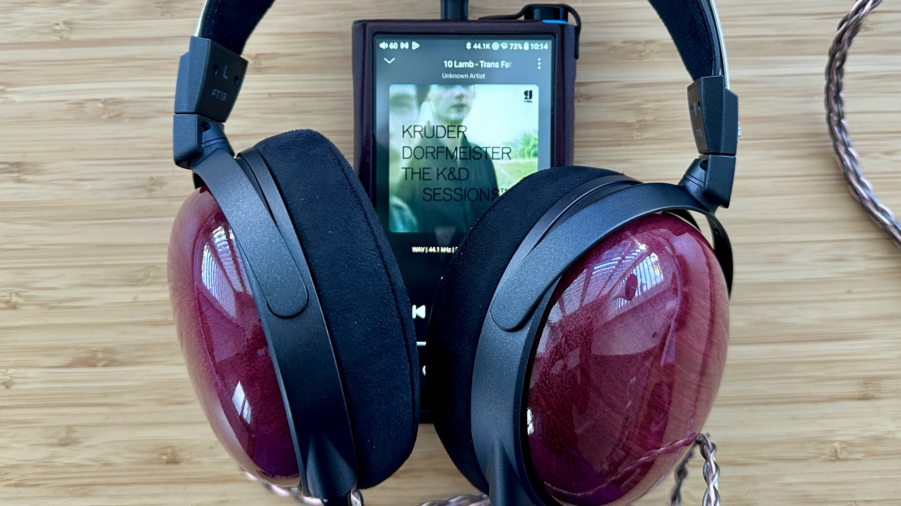 FiiO FT13 closed-back over-ear wired headphones connected to a portable music player on a wooden surface.