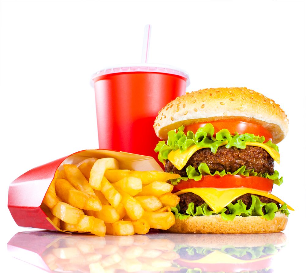 A fast food burger piled high with toppings sits beside a large pile of french fries.