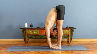A man stretches his wrists during a forward bend in yoga
