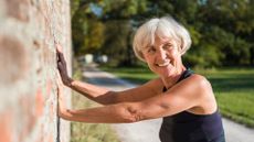 senior woman leans against a brick wall using her hands