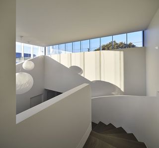 Sculptural staircase in a residential home featuring brown stairs and white banisters/walls with high windows and hanging white ball lighting