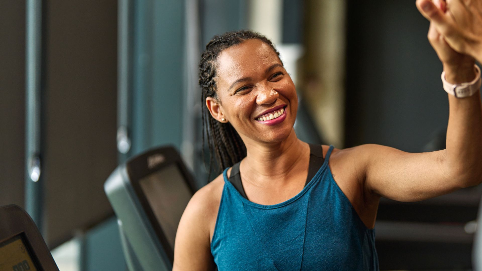 Woman high fiving after doing treadmill workout, smiling and wearing workout clothes