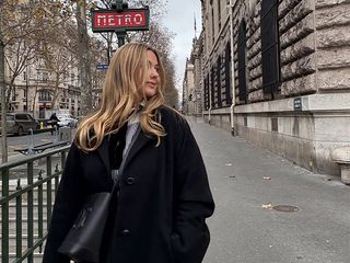 olivia wears black coat while posing on the streets of paris