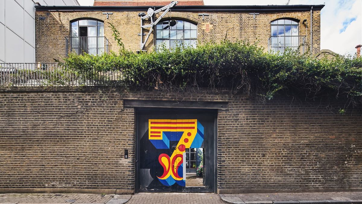 A tall brick wall in front of a house with a large metal door in the middle with the number 7 written onto it