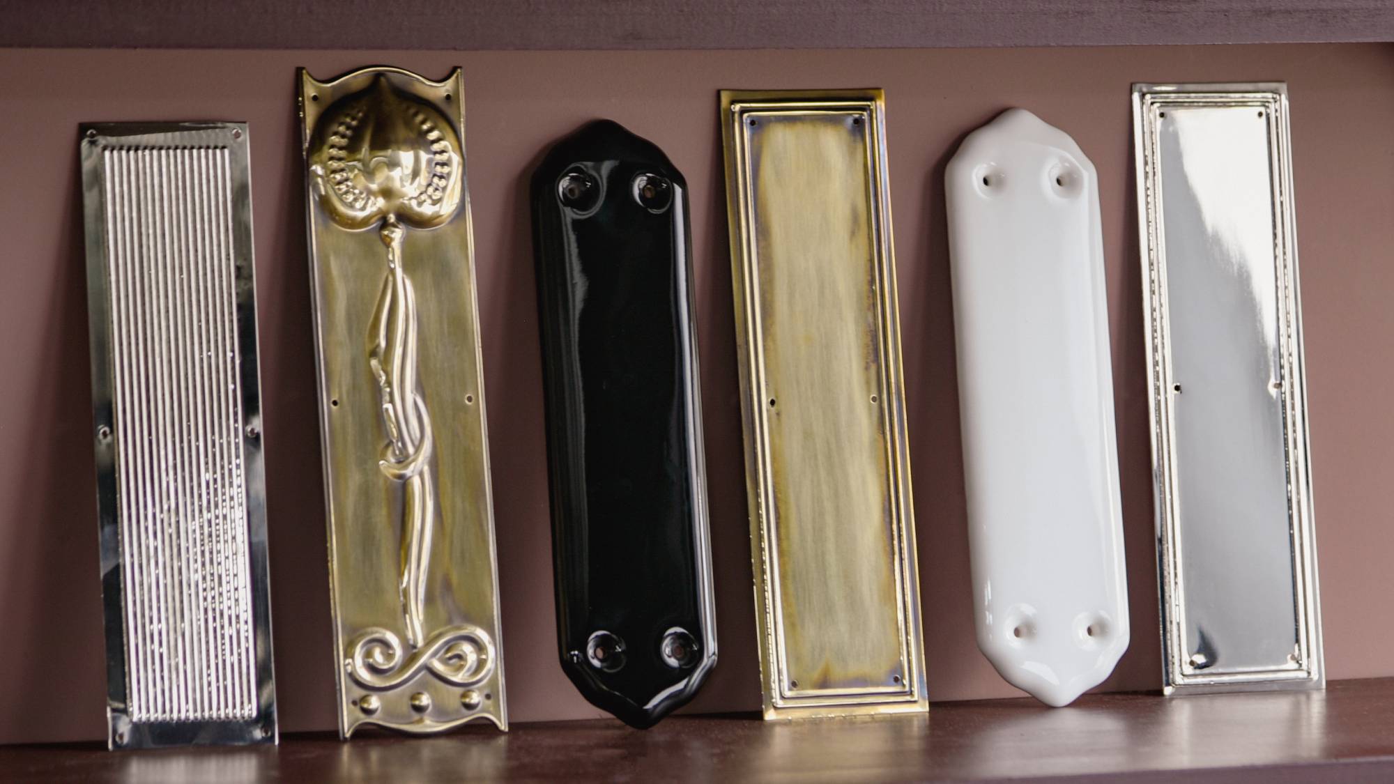 various fingerplates in different finishes and designs lined up against a wall