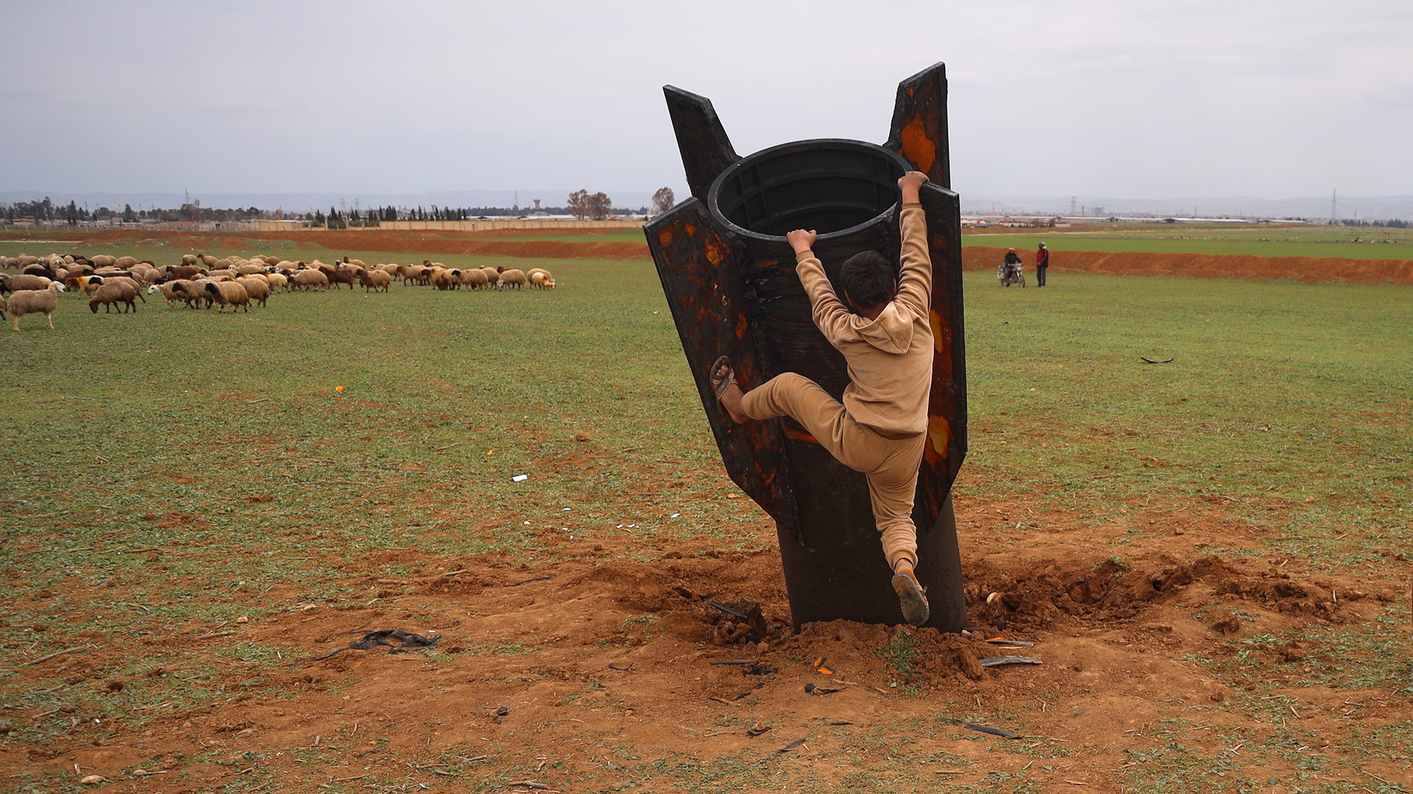 A boy climbs on an unexploded Iranian projectile that landed in a field on the outskirts of Qamishli, Syria
