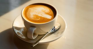 Flat white in white china cup sitting on wooden table