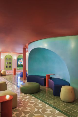 A cinema sitting area with pink and blue walls, round chairs, wall sofas and patterned floor tiles.