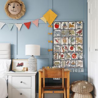 a toddler's bedroom with blue panelled walls, colourful bunting, desk and animal motifs