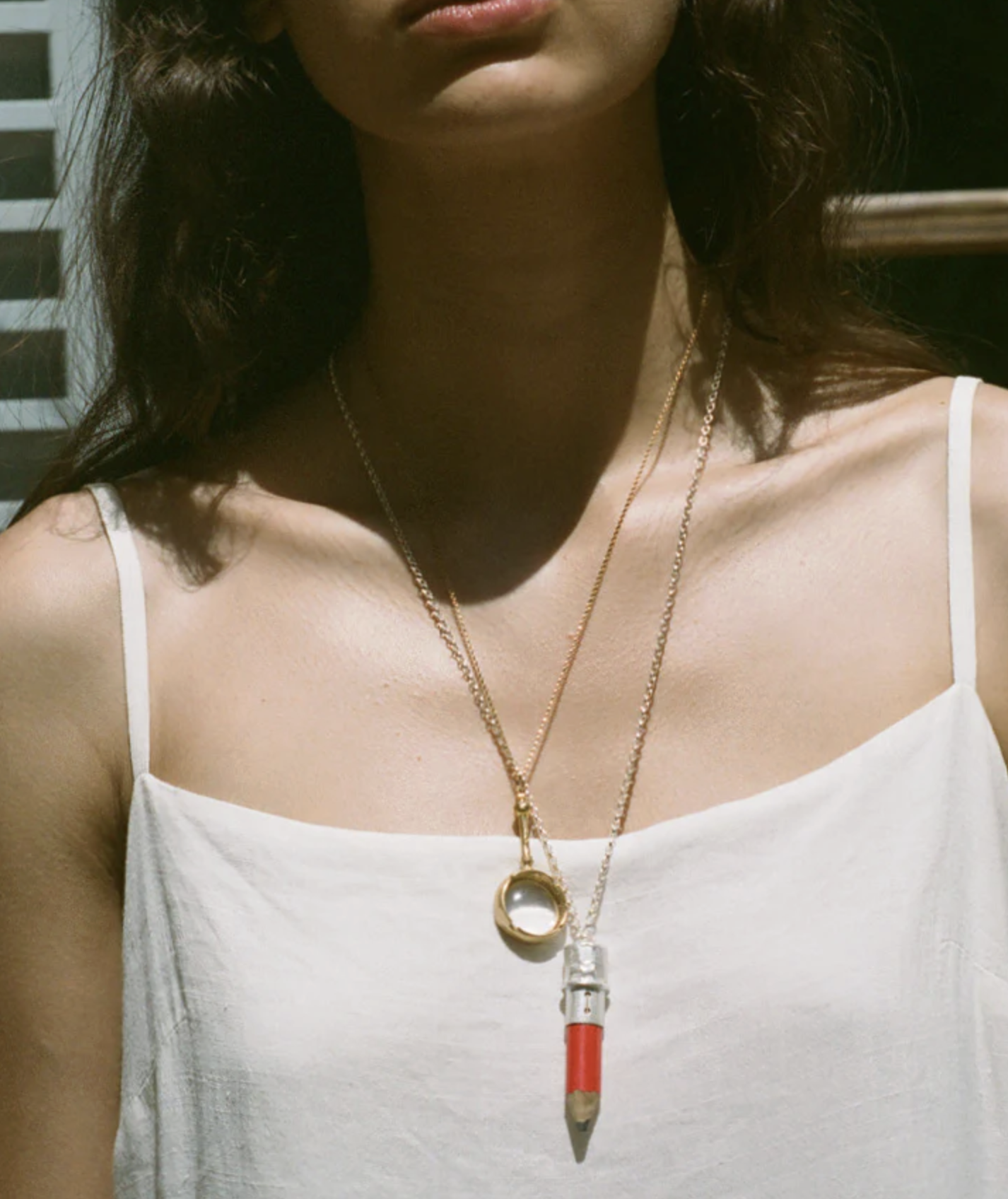 Alighieri model wears gold ring necklace, silver pencil necklace white cami top