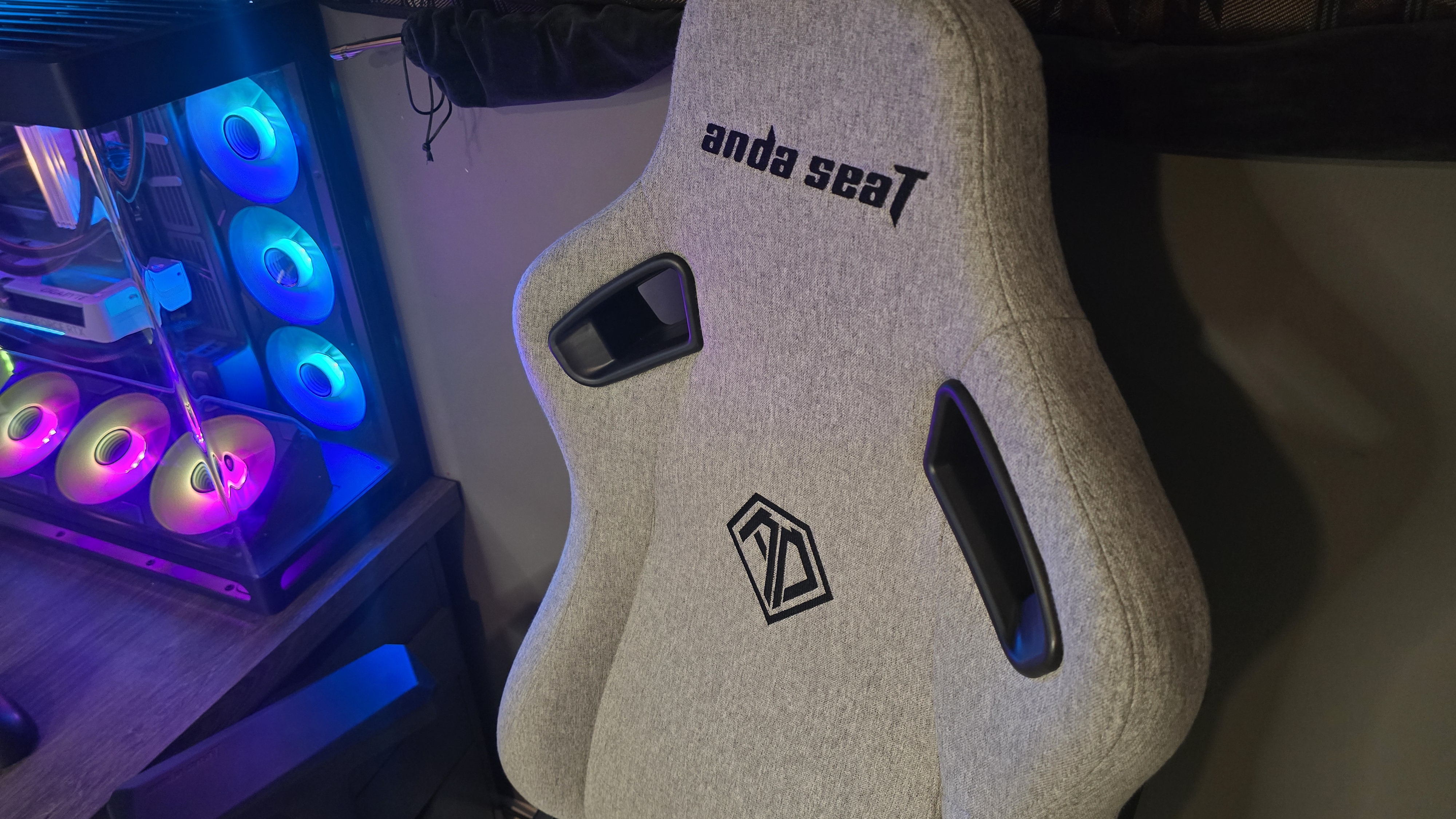 A grey gaming chair beside a pink and blue-lit gaming PC case