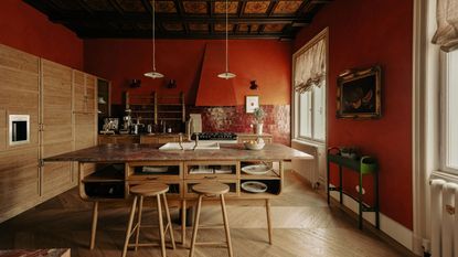 A kitchen with paprika red walls, burgundy wall tiles, wooden cabinetry, wooden floors, and a wood freestanding island