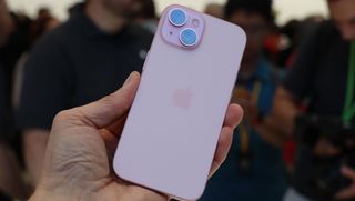 En hand håller upp en ljusrosa iPhone 15 med baksidan vänd mot kameran.