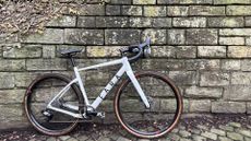 The white Fara F/Grave bike lent up against a stone wall on cobbles 