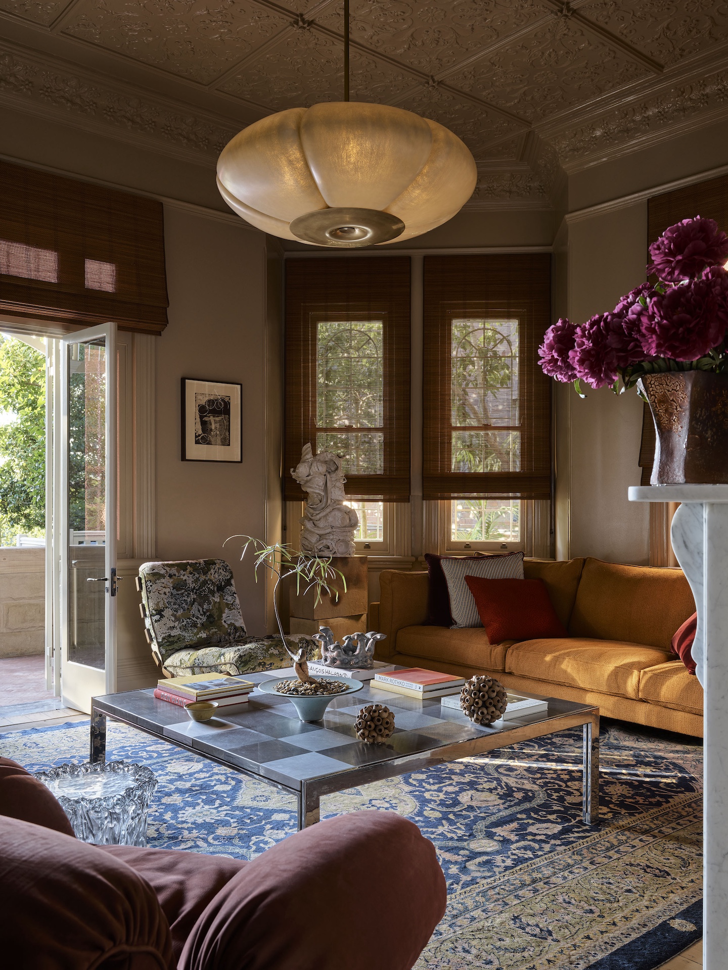 modern living room with bamboo blinds, Persian-style rug, chrome table decorated with a potted plant and books, orange sofa, and low pendant light