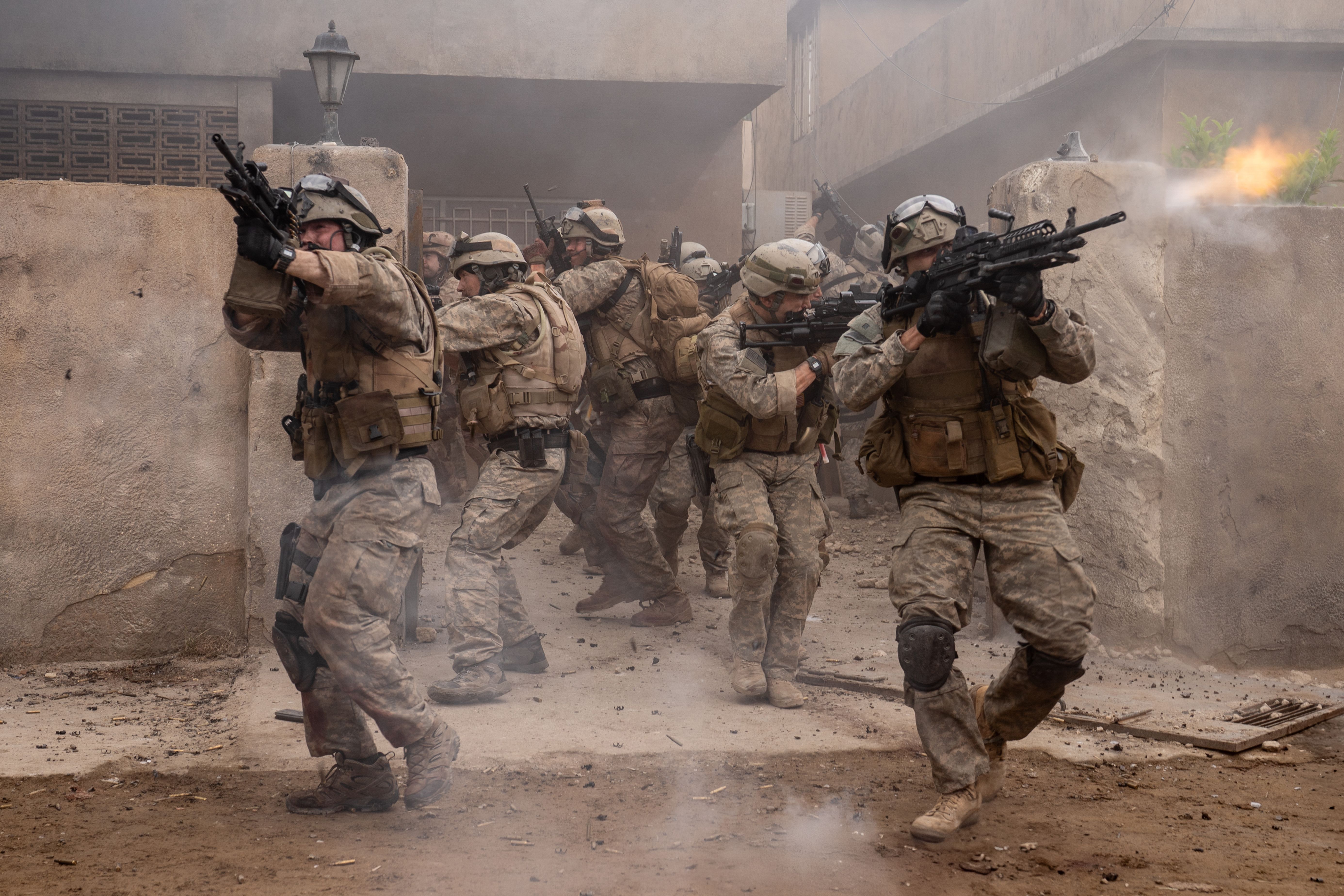 A group of soldiers in full gear coming out of a building firing on enemies.
