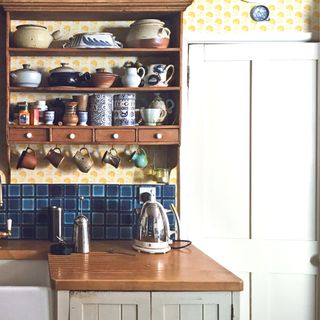 yellow wallpaper in kitchen with open wooden shelving and blue tiled splashback