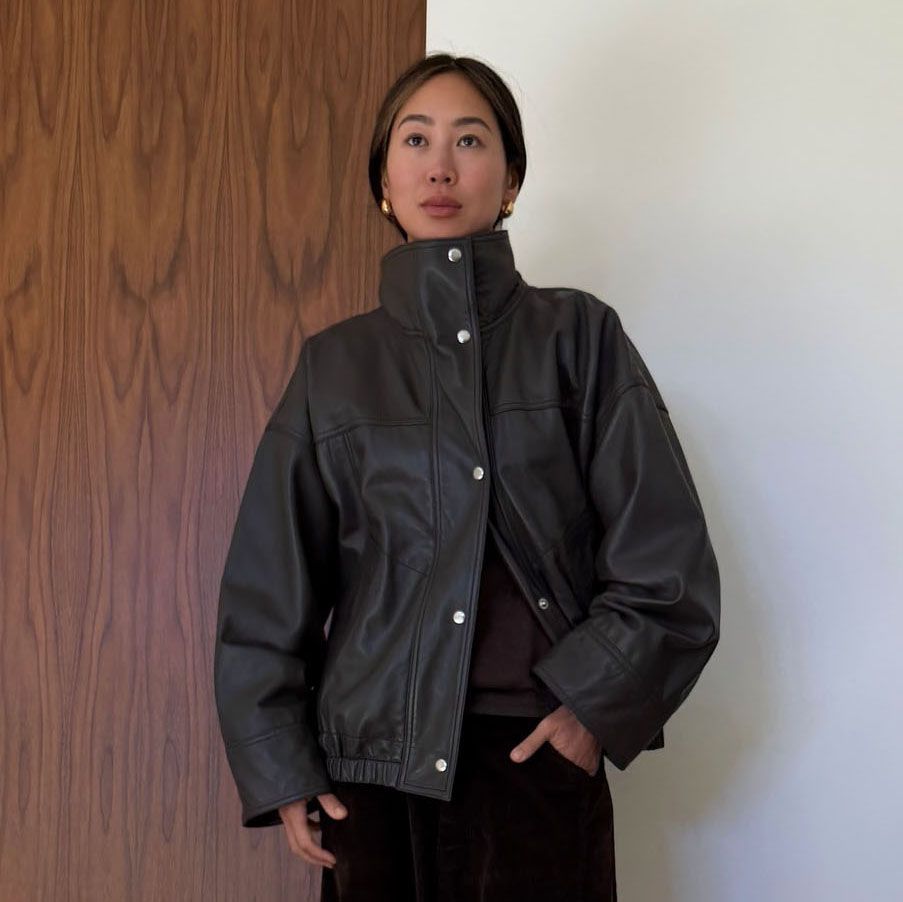 a woman wearing a brown leather jacket and black pants 