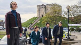 Patience, wearing headphones, stands away from Bea Metcalf (Laura Fraser), Will Akbari (Ali Ariaie) and Jake (Nathan Welsh), with York Castle in the background, in Patience