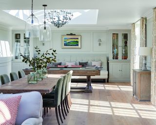 dining room with lilac sofa, wooden table, green dining chairs, pool table and upholstered bench, chandelier and pendant lights