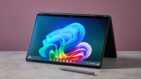 Three-quarter view of HP OmniBook Ultra Flip 14 folded back and propped up on white desk, with stylus in front and pink wall in background